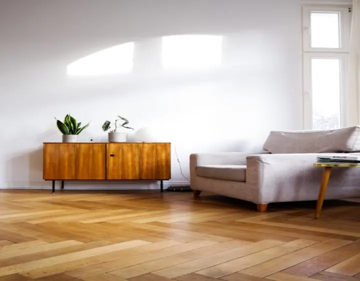 Séjour lumineux : parquet à chevrons clair, enfilade en bois et fauteuil blanc.