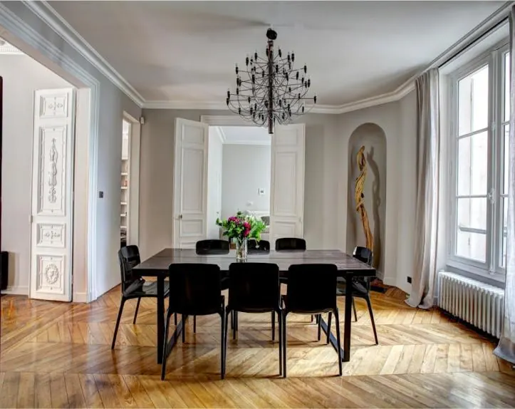 Salle à manger haussmannienne : parquet à chevrons, lustre, moulures et table noire.