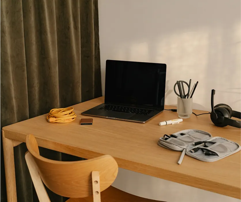 Poste de travail : plateau en bois clair, ordinateur portable, chaise en bois cintré devant un rideau.