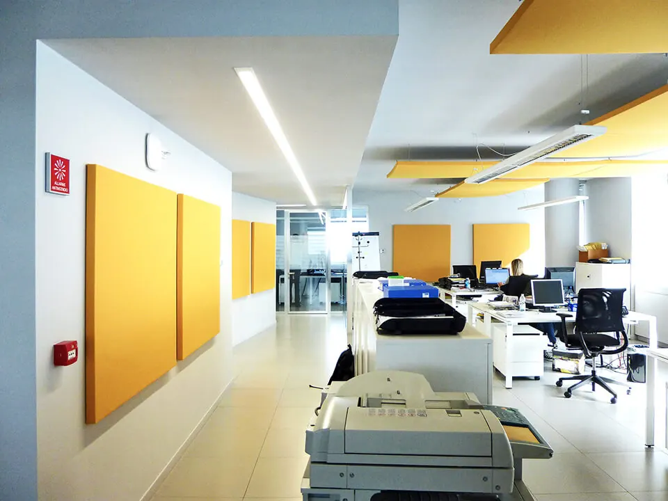 Plateau de bureaux en open space : postes alignés, panneaux acoustiques jaunes, sol clair.