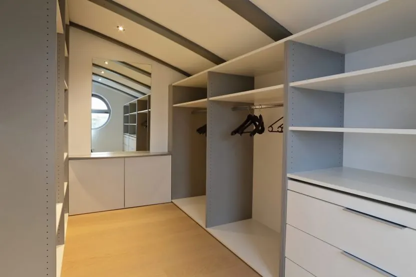 Dressing sur mesure : penderies, étagères et tiroirs blancs, miroir rond, sol clair.